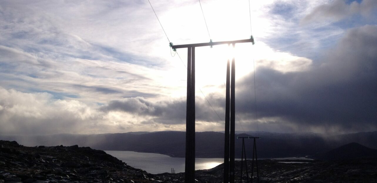 Strømstolper leder strømlinjen ned fjellsiden med en skyet himmel i bakgrunnen