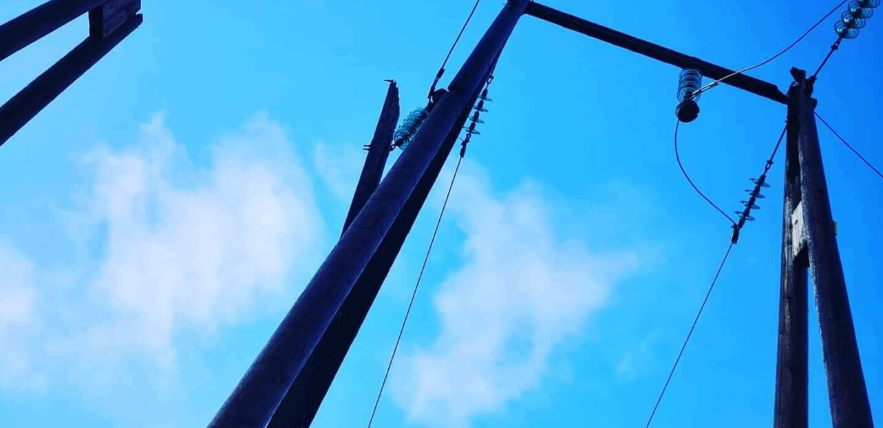 Knekt strømstolpe sett fra bakkenivå med blå himmel i bakgrunnen